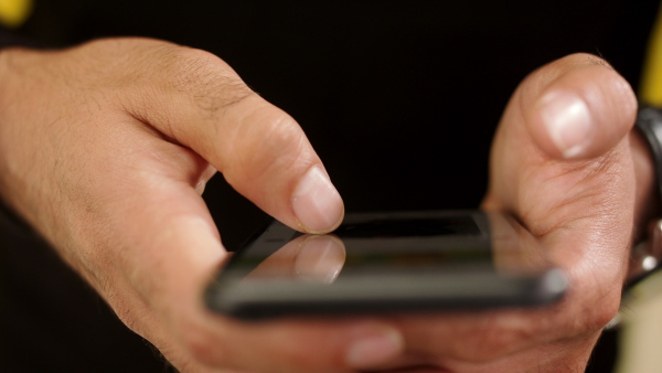 Close up of unrecognizable man using black smartphone in a studio on yellow background.