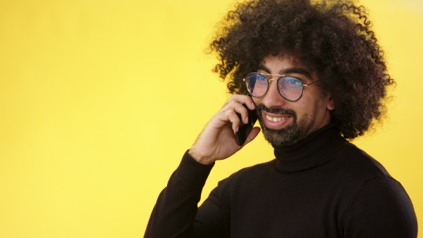 Portrait of cheerful mature man with smartphone in a studio on yellow background.