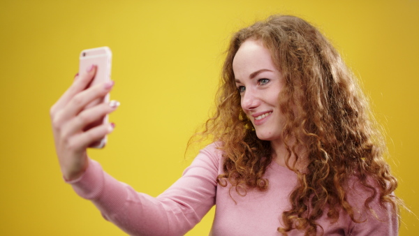 Portrait of young woman with smartphone taking a selfie in a studio.