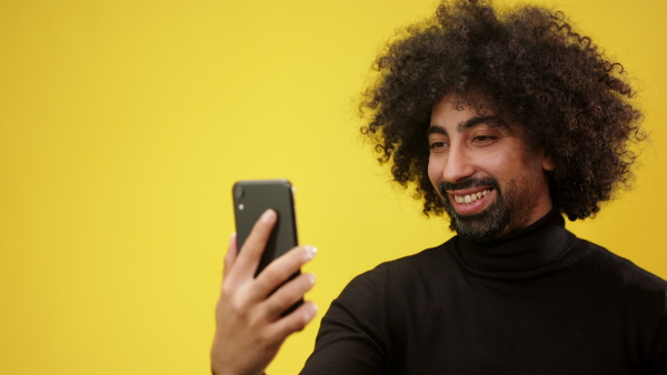 Portrait of mature man with smartphone taking selfie in a studio on yellow background.