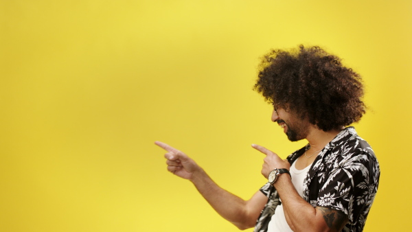 Portrait of young man with curly hair in a studio on yellow background, pointing fingers.