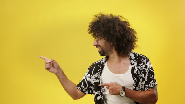 Portrait of young man in a studio on yellow background, spinning, pointing fingers and looking at camera.