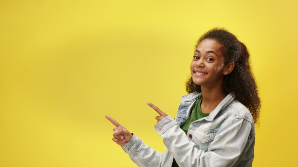 Portrait of beautiful teenager girl in a studio on yellow background, pointing finger.