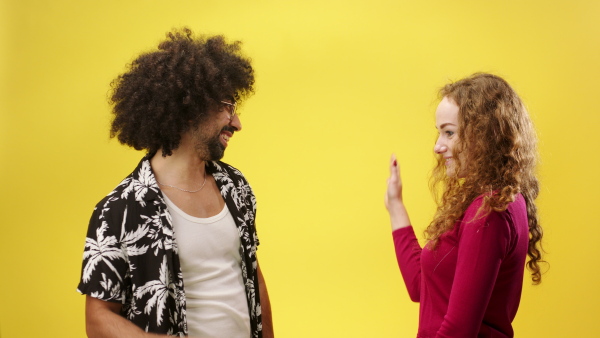 Portrait of mature man and young woman in a studio on yellow background, giving high five.