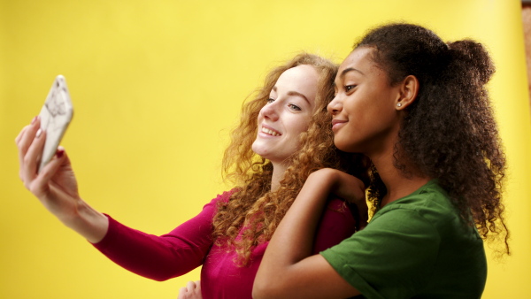 Portrait of young woman with teenager girl in a studio on yellow background, taking selfie.