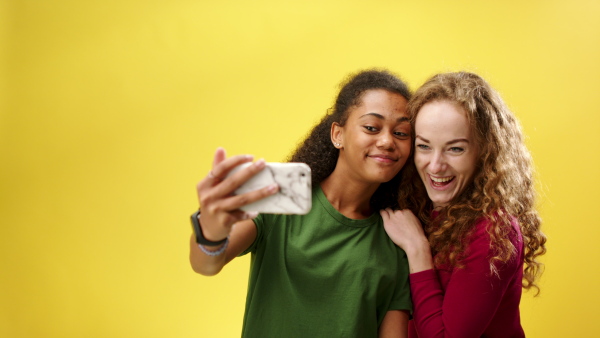 Portrait of young woman with teenager girl in a studio on yellow background, taking selfie.