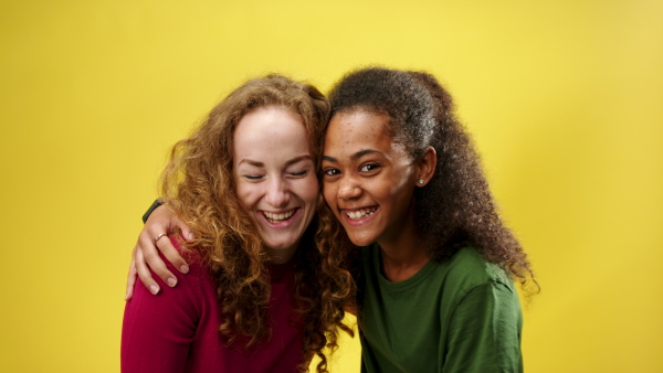 Portrait of young woman with teenager girl in a studio on yellow background hugging then looking at camera.