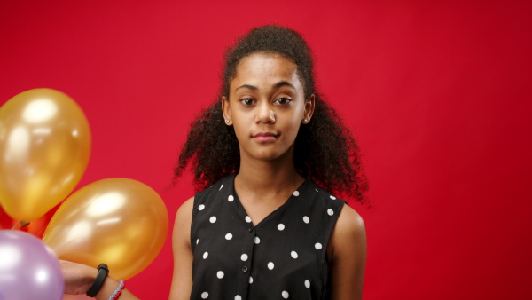 Young teenager girl with balloons in a studio on red background, looking at camera.