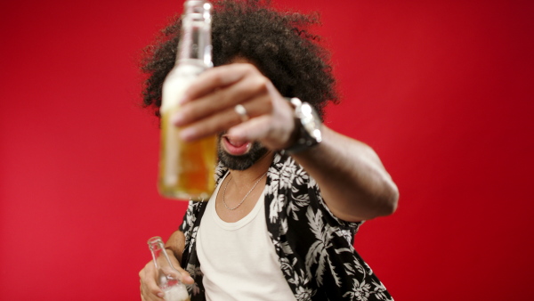 Portrait of young man celebrating with beer bottles in a studio on red background, looking at camera.