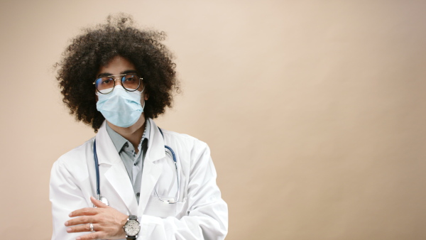 Sad mature man doctor with face mask standing in studio looking at camera, coronavirus concept. Copy space.