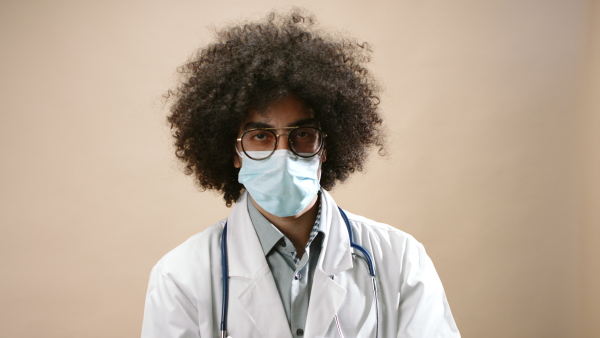 Sad mature man doctor with face mask in standing in studio, coronavirus concept. Copy space.