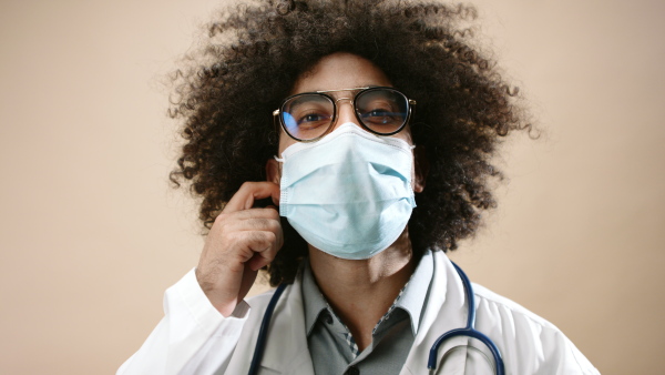 Mature man doctor with face mask standing in studio looking at camera, coronavirus concept. Copy space.