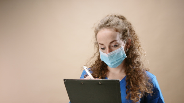 Young woman doctor in a studio holding clipboard and looking at camera, coronavirus concept.