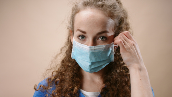 Young woman doctor in a studio taking off face mask, looking at camera. Coronavirus concept.