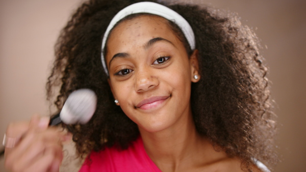 Portrait of teenage girl in a studio applying make-up, beauty concept.