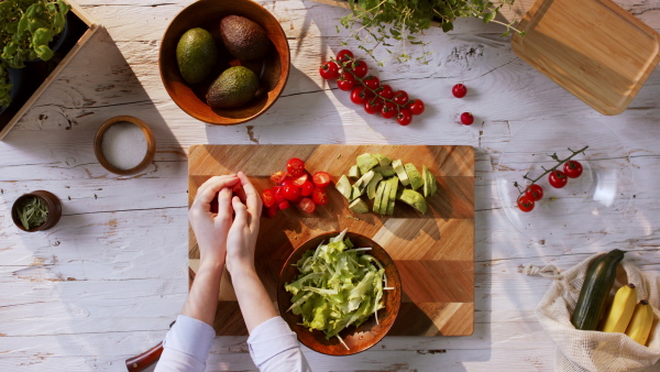 Top view of unrecognizable young woman making a vegetable salad.