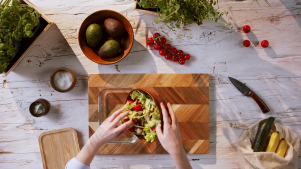 Top view of unrecognizable young woman making a vegetable salad.