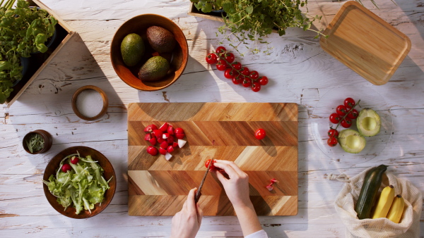 Top view of unrecognizable young woman making a vegetable salad.