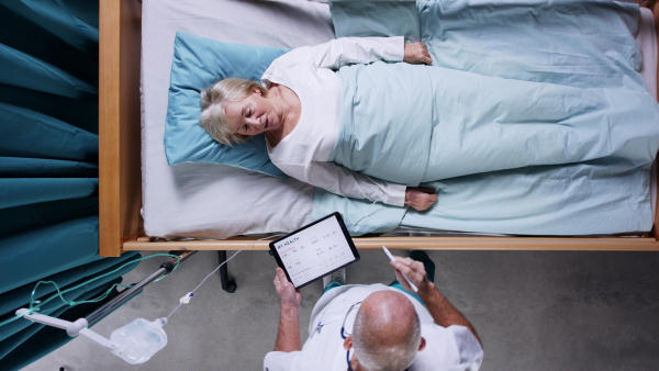 A top view of doctor with tablet examining patient in bed in hospital. Copy space.