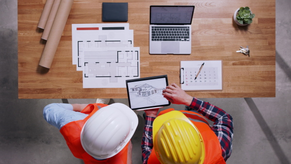 Top view of two architects with tablet in hardhats discussing about project. Copy space.