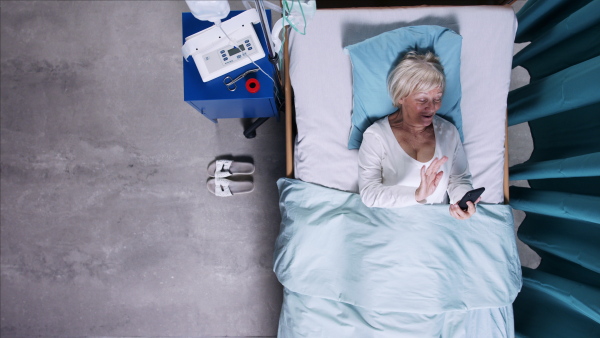 Top view of woman covid-19 patient with mask using smartphone in bed in hospital, coronavirus concept.