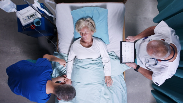 A top view of doctors with stethoscope examining patient in bed in hospital. Copy space.