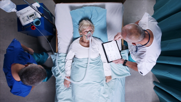 A top view of doctors with stethoscope examining patient in bed in hospital. Copy space.