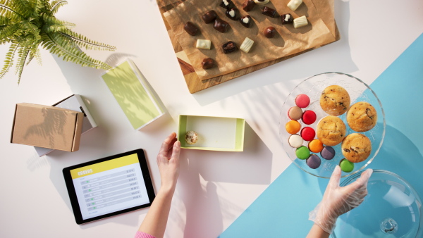 A top view of unrecognizable woman packing biscuits, processing orders desktop concept.