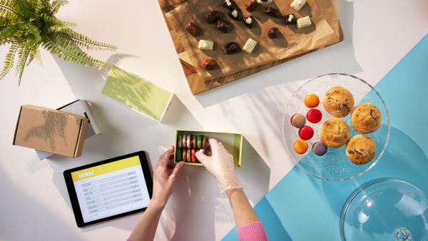 A top view of unrecognizable woman packing biscuits, processing orders desktop concept.