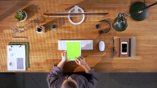 A top view of designer working on computer and tablet with green screen at desk in home office.