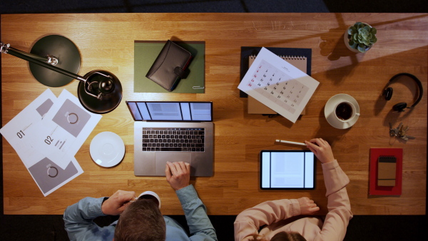 A top view of businessman working on computer with colleague at desk in home office.