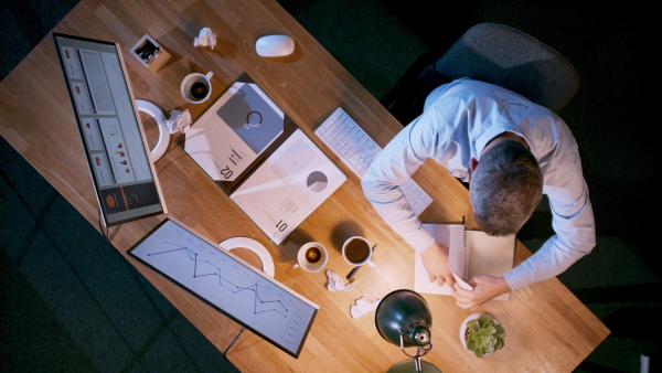 A top view of businessman working on computer at desk with paperwork in home office.