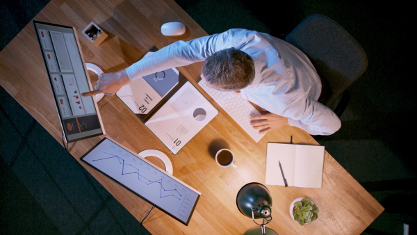 A top view of businessman working on computer at desk with paperwork in home office, celebrating.