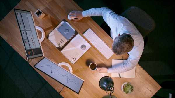 A top view of businessman working on computer at desk with paperwork in home office.