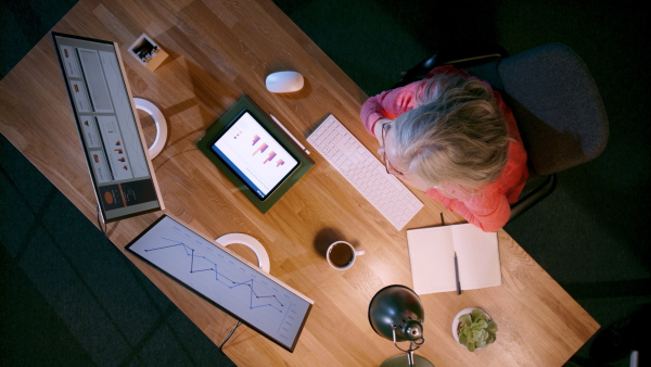 A top view of businesswoman working on computer at desk with paperwork in home office, celebrating.