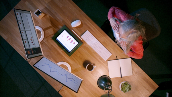 A top view of businesswoman working on computer at desk with paperwork in home office, celebrating.