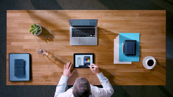 A top view of creative businessman working on laptop computer at desk with paperwork in home office.