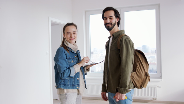 Happy young couple with tablet moving and planning in new flat, looking at camera. New home and relocation concept.