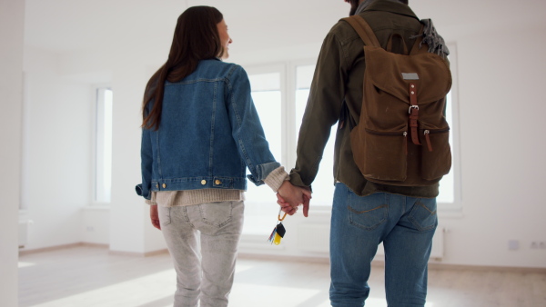 A rear view of young couple with keys moving in new flat, new home and relocation concept.