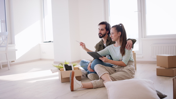 Side view of happy young couple with tablet moving and planning in new flat, new home and relocation concept.