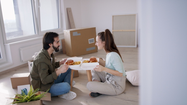 Side view of young couple with hamburgers and boxes moving in new flat, new home and relocation concept.