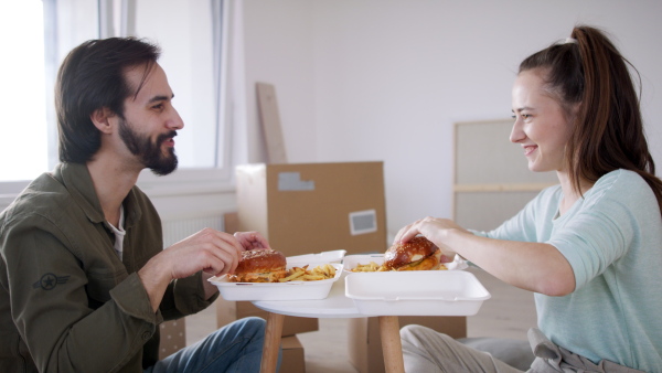 Side view of young couple with hamburgers and boxes moving in new flat, new home and relocation concept.