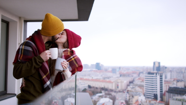 Happy young couple owners with coffee on balcony, kissing. New home and relocation concept.