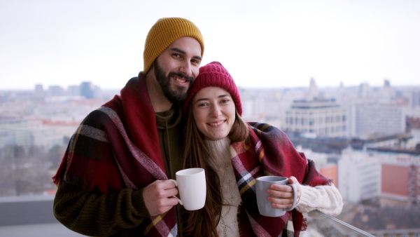 Happy young couple owners with coffee on balcony in new flat, moving in, looking at camera. New home and relocation concept.