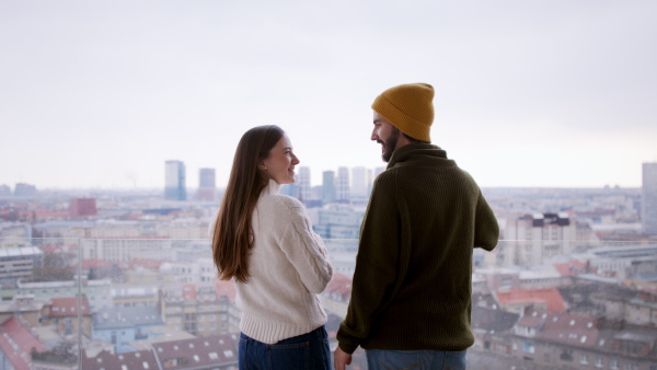 Rear view of happy young couple owners with coffee on balcony in new flat, moving in, new home and relocation concept.