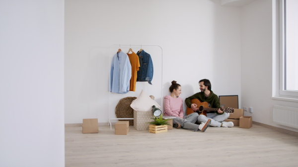 Happy young couple with boxes and guitar moving in new flat, new home and relocation concept.