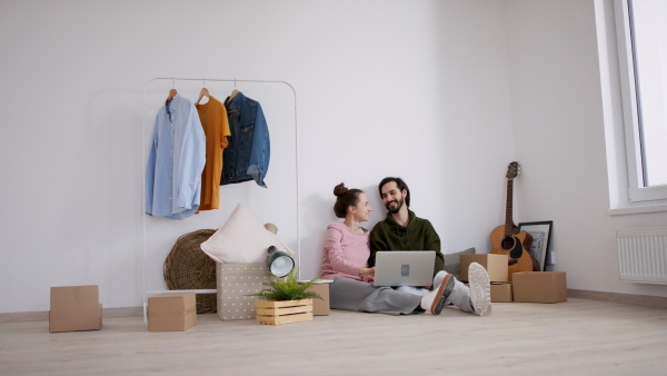 Happy young couple with laptop and boxes moving in new flat, new home and relocation concept.