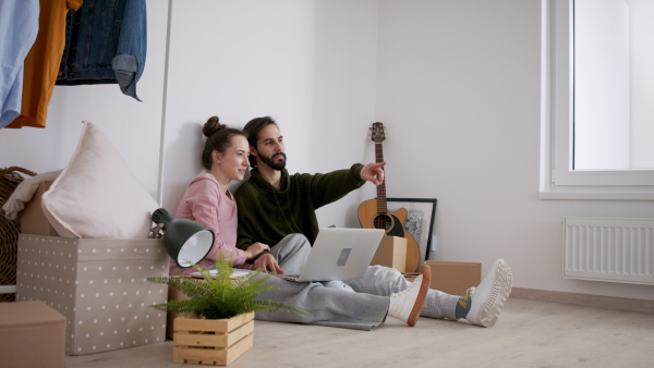 Happy young couple with laptop and boxes moving in new flat, new home and relocation concept.