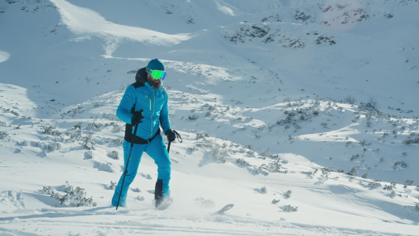 A male backcountry skier hiking to the summit of a snowy peak in the Swiss Alps