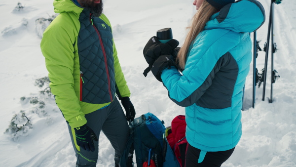 A skier couple taking break and drink tea during skiing in mountains.